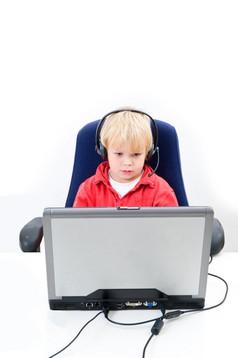 年轻的男孩坐着后面移动PC穿耳机与麦克风垂直图像