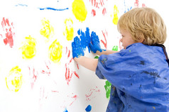 年轻的男孩紧迫的他的手覆盖与蓝色的油漆对墙使打印与手指油漆