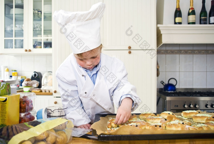 小男孩穿着老板配菜的甜蜜的面包烤凌乱厨房