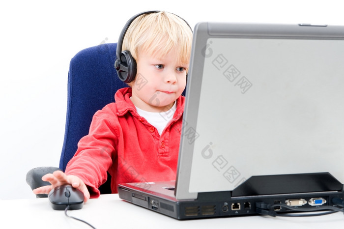 年轻的男孩坐着后面移动PC点击computermouse同时看的屏幕而且穿耳机