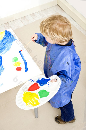 年轻的男孩站下一个表格与大表纸纸板表面与调色板与海报油漆他的手绘画交通光