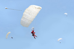 牙跳与降落伞在着陆与几个其他跳伞的背景对蓝色的天空