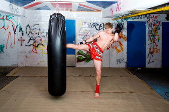 泰拳泰国战斗机给高踢在练习轮与拳击袋城市地下室