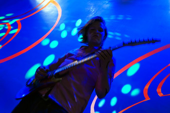 吉他手投蓝色的光与迷幻光影响的墙后面他