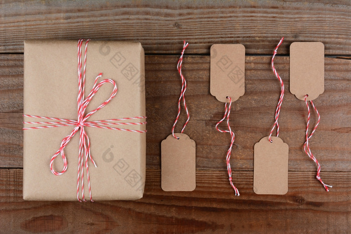 开销拍摄圣诞节包包装平原棕色（的）纸而且领带与红色的而且白色字符串四个空白标签是下一个的礼物黑暗乡村木表格