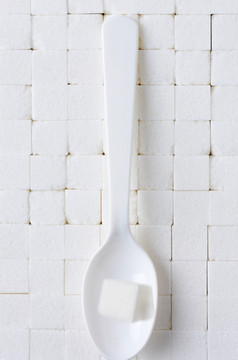 白色塑料勺子与单糖多维数据集背景密切堆放白色糖多维数据集