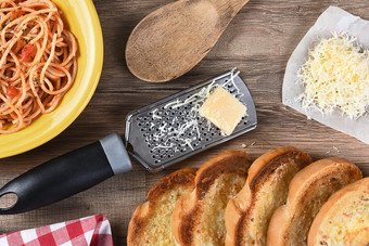 开销视图厨房表格与板意大利面大蒜面包磨碎的帕尔玛奶酪刨丝器木勺子红色的网纹餐巾