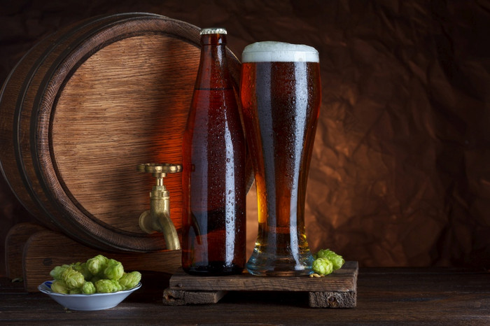 瓶装和不寻常啤酒玻璃与桶和新鲜的啤酒花为酝酿静物