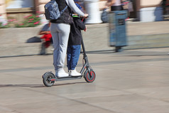 妈妈。和儿子骑电踢踏板车的城市广场模糊运动