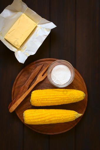开销拍摄两个玉米穗轴煮熟的甜蜜的玉米木板与盐而且餐具与一块黄油以上拍摄黑暗木与自然光