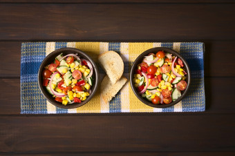 开销拍摄两个碗新鲜的蔬菜沙拉使甜蜜的玉米樱桃番茄黄瓜红色的洋葱红色的胡椒细香葱与烤面包的一边拍摄黑暗木与自然光