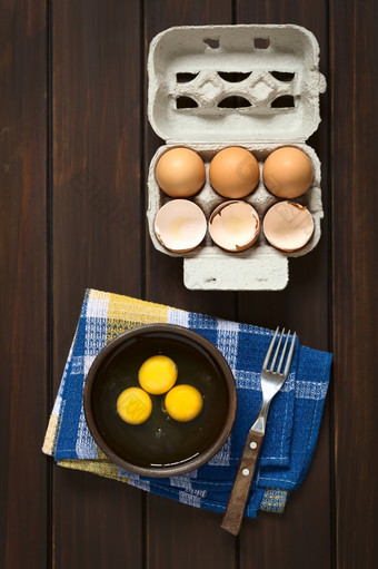 开销拍摄三个生鸡蛋乡村碗与叉的一边而且蛋盒子与鸡蛋而且蛋壳以上拍摄黑暗木与自然光