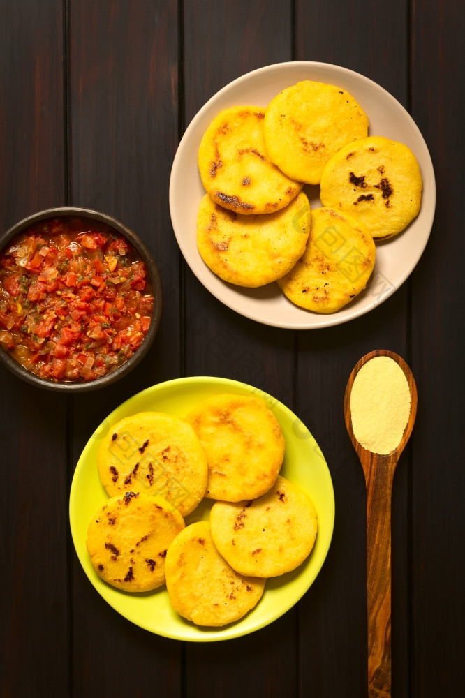 开销拍摄arepas盘子与哥伦比亚霍高酱汁番茄而且洋葱煮熟的碗Arepas是使黄色的白色玉米餐而且是传统上吃哥伦比亚而且委内瑞拉拍摄黑暗木与自然光哥伦比亚阿雷帕与霍高酱汁