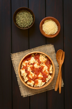 煮熟的意式馄饨与自制的番茄酱汁木碗与磨碎的奶酪而且干牛至小碗木勺子而且叉的一边拍摄开销黑暗木与自然光