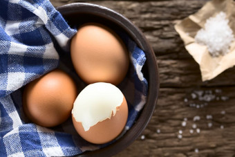 煮熟的棕色（的）鸡蛋碗与粗盐的一边拍摄开销木非常浅深度场焦点的前的去皮蛋煮熟的棕色（的）鸡蛋