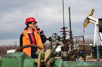 女人工程师的石油场会说话的的广播穿红色的头盔和橙色工作衣服工业网站背景石油和气体行业工程师