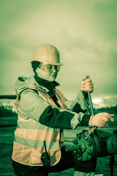 女人工人的石油场修复石油和气体好吧与的扳手穿头盔和工作衣服工作过程石油井口健美的