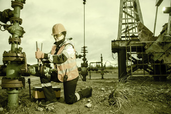 女人工人的石油场修复石油和气体好吧与的扳手穿头盔和工作衣服工作过程石油井口