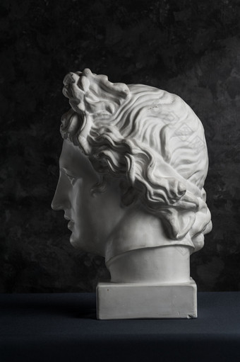 白色石膏复制古老的雕像阿波罗神太阳头为艺术家黑暗变形背景石膏雕塑男人。脸石膏复制古老的雕像阿波罗头黑暗变形背景石膏雕塑男人。脸