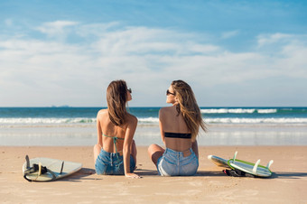 两个美丽的女朋友的海滩坐着的沙子关闭她的<strong>冲浪</strong>板而看的海洋