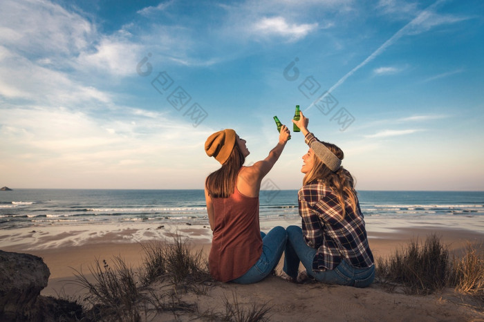 两个最好的朋友坐着的海岸线敬酒友谊