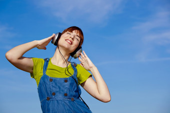肖像快乐女人听音乐在美丽的蓝色的天空