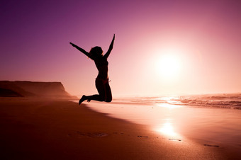图片女轮廓年轻的女孩跳的海滩的日落