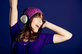 美丽的和快乐年轻的女人听音乐与耳机在紫罗兰色的背景