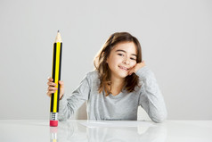 美丽的小女孩桌子上玩与大铅笔对灰色的背景