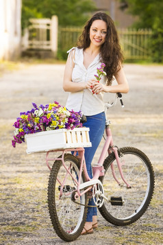 美丽的年轻的女人与她的自行车完整的野花