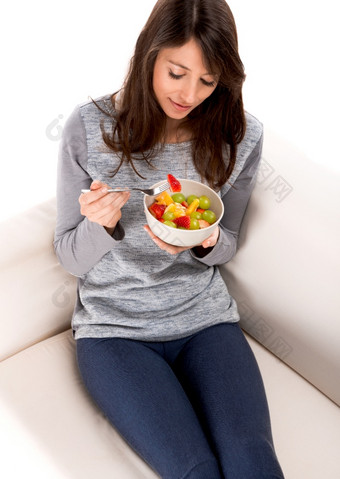 美丽的女人放松的沙发和吃水果沙拉放松与水果沙拉
