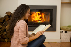 美丽的女人阅读书的温暖的壁炉