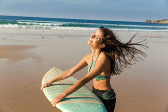 美丽的冲浪者女孩走在的海滩与她的冲浪板和微笑