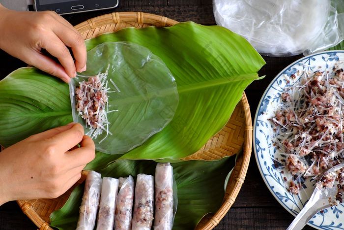 女人使春天卷父亲先生首页自制的食物填料从肉和包装器大米纸手滚动越南蛋卷绿色叶背景