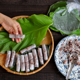 女人使春天卷父亲先生首页自制的食物填料从肉和包装器大米纸手滚动越南蛋卷绿色叶背景