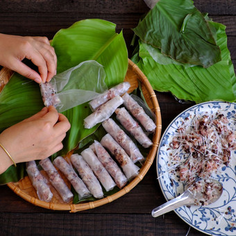 女人使春天卷父亲先生首页自制的食物填料从肉和包装器大米纸手滚动越南蛋卷绿色叶背景