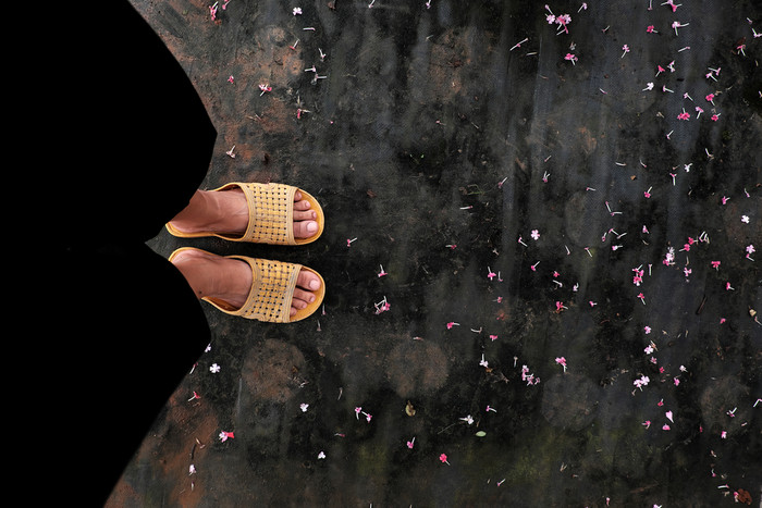 高视图场景与脚女人穿黑色的裤子和黄色的塑料凉鞋站地板上与小花花瓣秋天花园