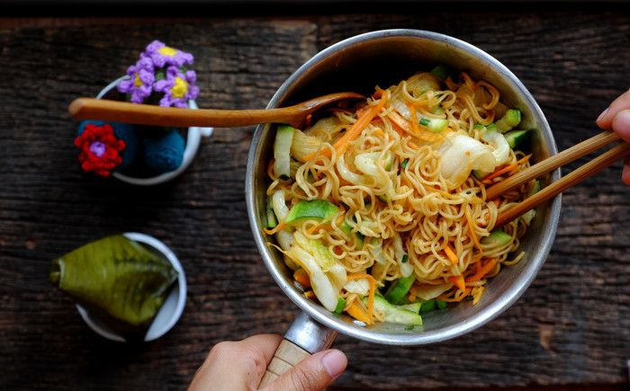 前视图关闭人类手混合黄色的干即时面条与蔬菜为快速素食主义者早餐黑暗木背景