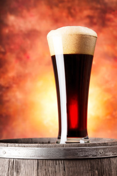 高玻璃黑暗啤酒与泡沫而且木桶橙色背景高玻璃黑暗啤酒与泡沫而且木桶