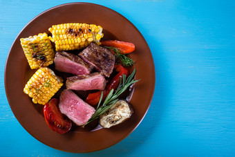 片炸肉与玉米和蔬菜板蓝色的背景视图从以上的概念自然传统的食物片炸肉与玉米和蔬菜板