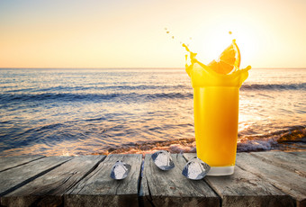 玻璃橙色汁与飞溅从橙色片和冰对的背景的海玻璃橙色汁站木表格对的背景海波日落玻璃橙色汁与飞溅从橙色片和冰