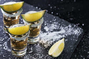 黑色的背景与龙舌兰酒眼镜分散与盐和石灰含酒精的鸡尾酒墨西哥传统的喝黑色的背景与龙舌兰酒眼镜分散与盐和