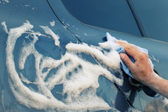 车洗与蓝色的海绵女手洗的机与肥皂泡沫爽肤水车洗与蓝色的海绵