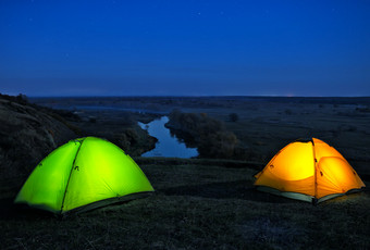 点燃从的内部橙色和绿色帐篷山以上的河晚上景观的概念自由隐私和旅行点燃从的内部橙色和绿色帐篷山以上箅