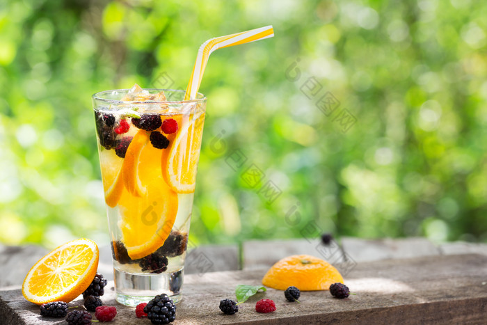 鸡尾酒柠檬水从橙色和浆果高玻璃夏天仍然生活玻璃与稻草站木表格在的浆果和橙色背景绿色树叶鸡尾酒柠檬水从橙色和浆果高玻璃