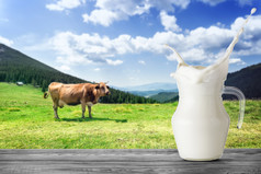 壶牛奶与飞溅的背景棕色（的）牛的山壶牛奶站木表格对的背景棕色（的）牛山牧场与绿色草壶牛奶与飞溅背景棕色（的）牛山