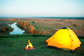 橙色点燃帐篷和篝火山以上的河秋天景观的概念隐私旅行和自由橙色点燃帐篷和篝火山以上的河