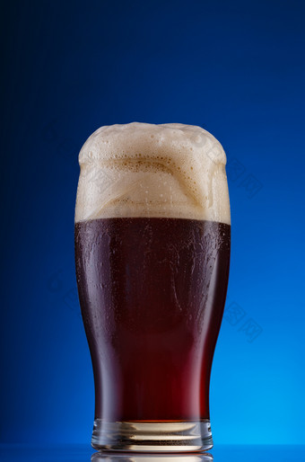 玻璃黑暗工艺啤酒与厚泡沫蓝色的背景玻璃黑暗工艺啤酒与泡沫蓝色的背景