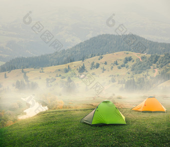 绿色和橙色帐篷平原的山多雾的早....夏天景观的概念自由孤独和旅行绿色和橙色帐篷平原山多雾的早....