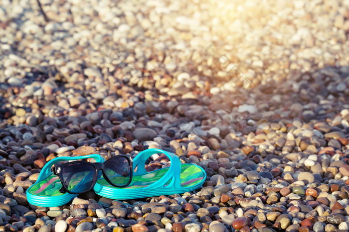 海滩蓝色的凉鞋和太阳镜的海滨石头假期和旅行概念海滩蓝色的凉鞋和太阳镜的海滨石头